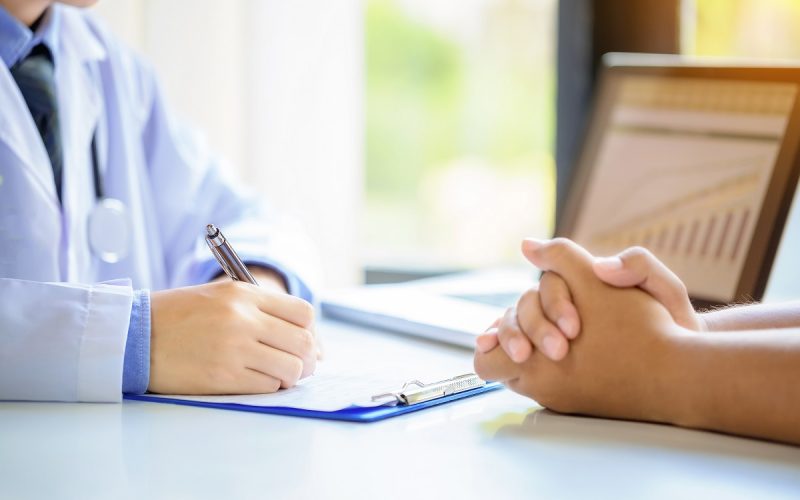 Doctor man consulting patient while filling up an application form at the desk in hospital. Medicine and health care concept